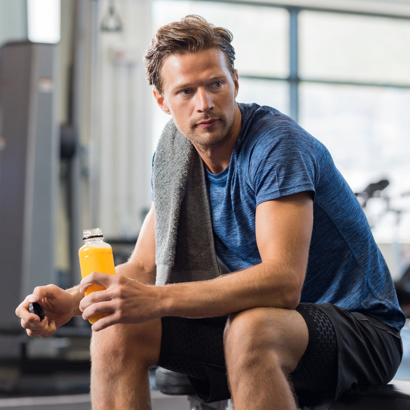 Man in a gym holding an orange juice bottle and a towel