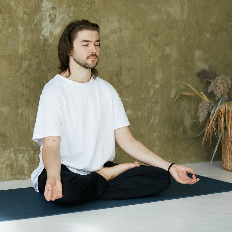 Man meditating on a yoga mat against a textured wall.